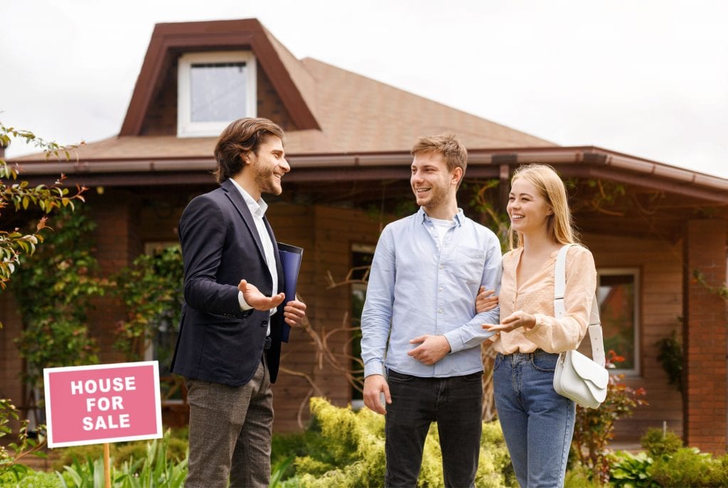 a happy couple is talking to a real estate agent about a house that is for sale